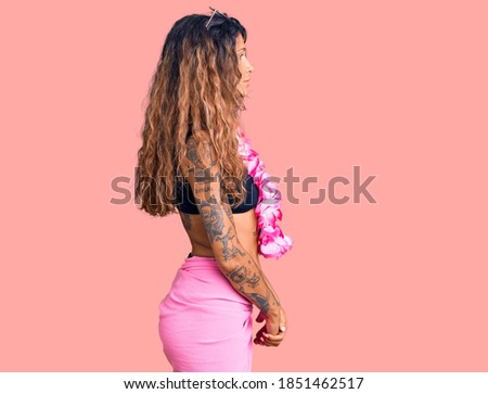 Young hispanic woman with tattoo wearing bikini and hawaiian lei looking to side, relax profile pose with natural face with confident smile. 
