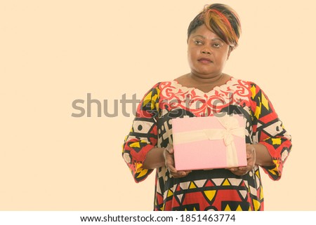 Studio shot of fat black African woman holding gift box while thinking