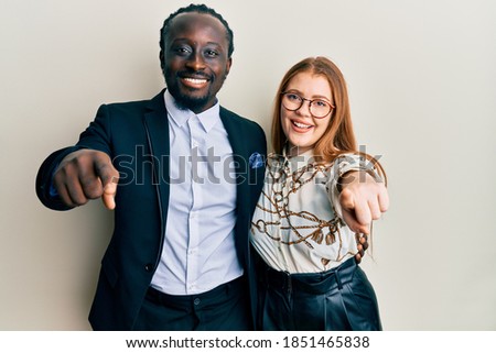 Young interracial couple wearing business and elegant clothes pointing to you and the camera with fingers, smiling positive and cheerful 
