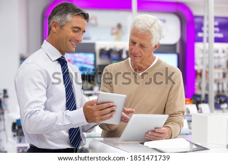 A salesman showing a digital tablet to an elderly man in an electronics store.