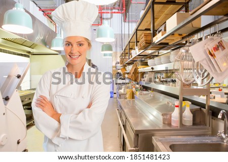 Young chef standing in the kitchen with arms crossed wearing a clean white chef's uniform