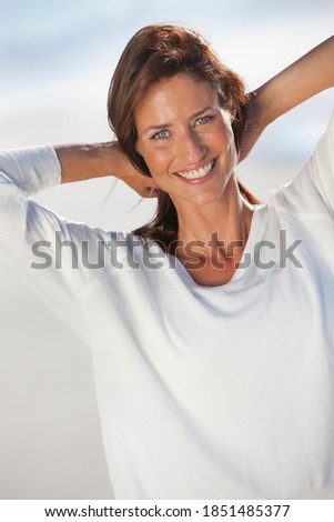 Portrait shot of woman smiling at the camera with her hands behind head on a sunny beach.
