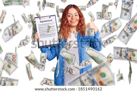 Young latin woman holding clipboard with agreement document smiling happy and positive, thumb up doing excellent and approval sign