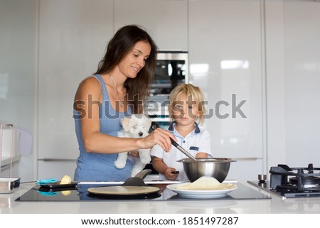 Cute toddler child and mom, mother and blond boy, making pancake in kitchen, eating them