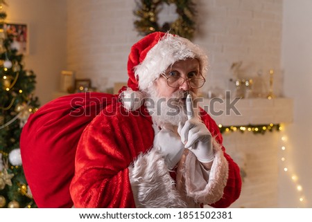 Traditional Santa Claus holding a bag with presents at home near christmas tree and fireplace. Christmas spirit, magic, dream concept
