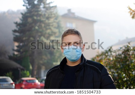 People with face mask. Concept with copy space. Portrait of young man at the street. Photo outdoors in a city. Back to school. School-age boy with a protective medical mask on her on his face.