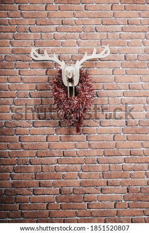 Wooden deer hanging on the wall decorated with christmas garlands. Vertical picture