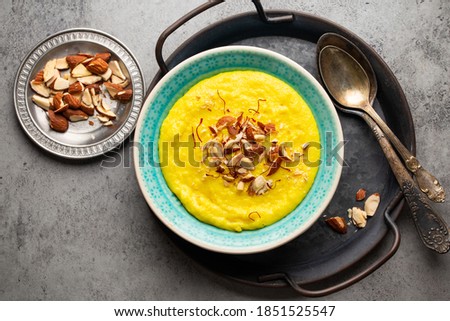 Traditional Indian dish Kheer, sweet rice milk pudding with almonds and saffron in blue ceramic bowl with spoons on stone rustic background, top view. Dessert meal of Indian cuisine  Royalty-Free Stock Photo #1851525547
