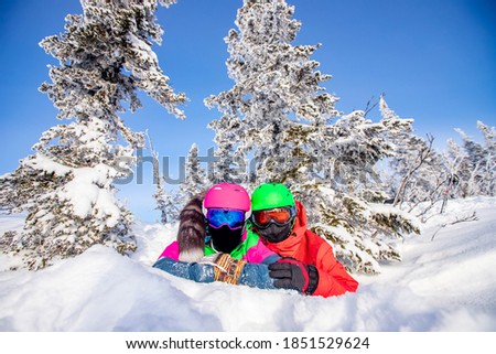 Two people in sportswear for snowboarding and skiing lying in snow against background forest and blue sky, have fun smile.