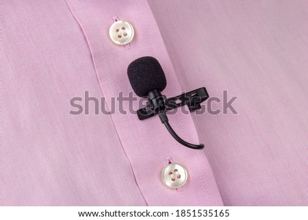 A clip-on lavalier microphone is attached to a pink shirt, close-up. Audio recording of the sound of the voice on a condenser microphone.
