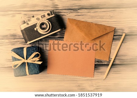 Gift box, old camera and blank paper card on vintage wooden background