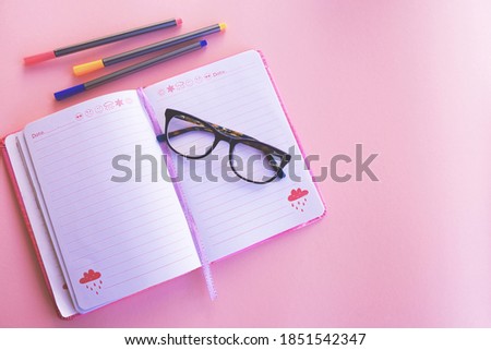 Flat composition with notebooks, colored pens and glasses, pink background.
