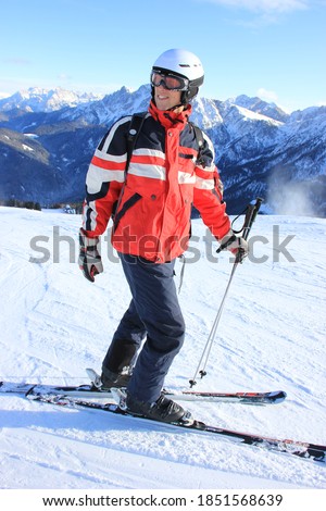 Young man in red black ski outfit and helmet, in front of blue sky and mountain background and snowy ground, skiing on the dolomite ski paradise "Kronplatz"