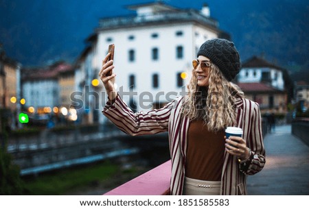 Beautiful blonde girl with cellphone on the bridge. Selfie and city background.
