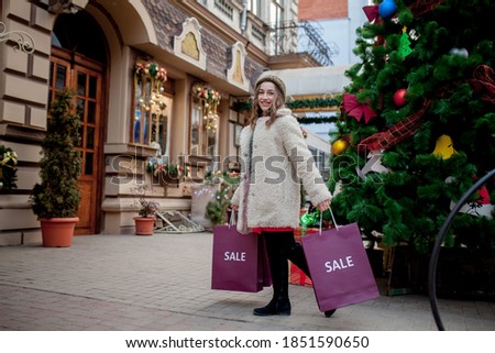 Happy woman holds paperbags with symbol of sale in the stores with sales at Christmas, around the city. Concept of shopping, holidays, happiness, Christmas Sales