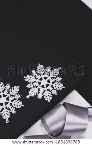 Christmas postcard, black and white background, grey ribbon and  white snowflakes.
