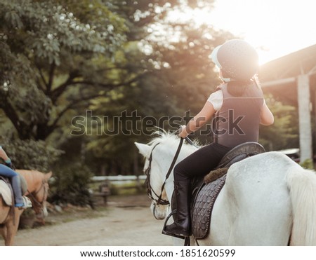 Horse rider.Back view Kids learn to ride a horse.Happy asian kid girl riding horse in horse school farm club.Horseback riding, lovely powerful equestrian.Cowgirl kid fun in farm.Kids Activity.Animals.