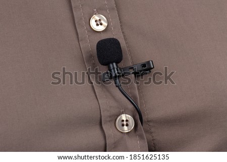 Audio recording of the sound of the voice on a condenser microphone. The lavalier microphone is secured with a clip on a brown women's shirt close-up.
