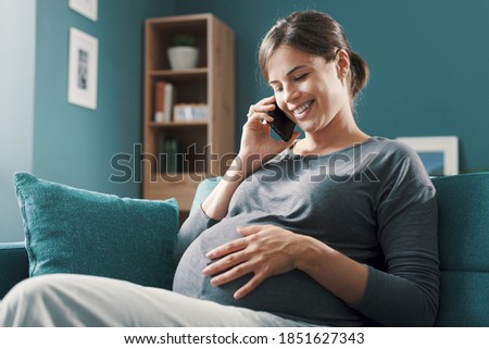 Happy young pregnant woman relaxing on the sofa at home and talking on the phone with her friends