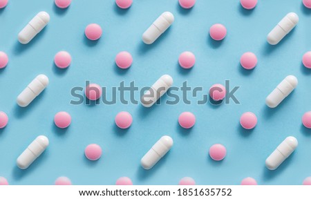 Scattered Pills on a blue background , Medicine concept. Multiple long and round white capsue and hard pills on a blue. Colorful pattern of pills and capsules on a blue. Seamless pattern