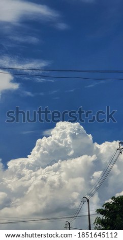 Wires and electric poles on the roadside. Behind there are large clouds in the sky.
