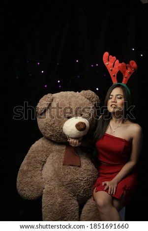 chinese woman holding bear doll using red dress with reindeer hat on grey background