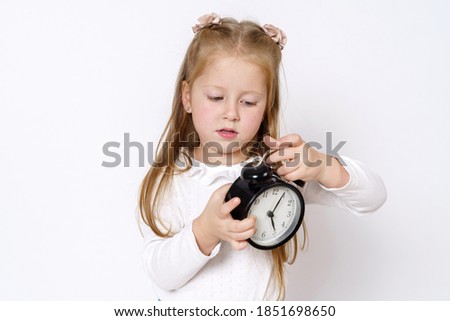 Children concept. A girl holds an alarm clock in her hands, plays with it. Isolated over white background.