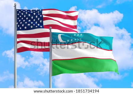 Uzbekistan and United States national flag waving in the windy deep blue sky. Diplomacy and international relations concept.