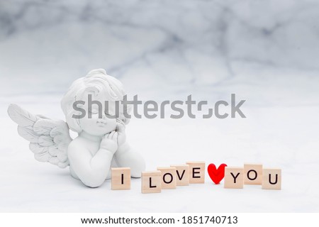 The word "i love you" and a cute angel on a white, marble background. Love on wooden cubes. Theme of love. Valentine's day. Wooden blocks with the word love. Positive emotion.