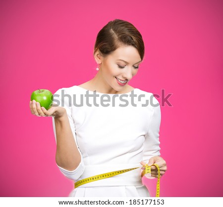 Closeup portrait young attractive, happy,  fit woman in white dress, holding green apple, measuring her waist, isolated magenta background. Healthy life style, nutrition. Positive emotion, expression