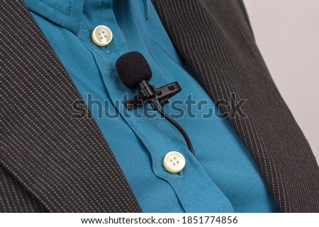 The lavalier microphone is secured with a clip on a blue women's shirt close-up. Audio recording of the sound of the voice on a condenser microphone.

