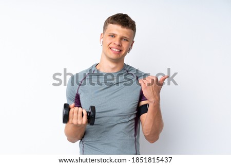 Young sport man with weightlifting over isolated white wall pointing to the side to present a product