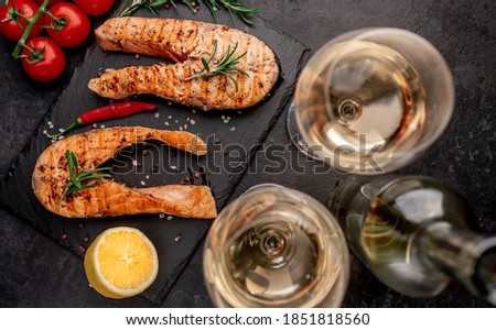 Dinner for two. Grilled salmon steaks, bottle of wine and glasses on stone background. View from above