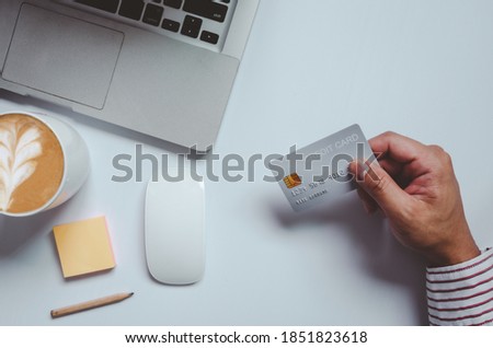 Top view man holding a credit card and on the desk. Laptop computer Notepad and pen.Online shopping business, pay by credit card