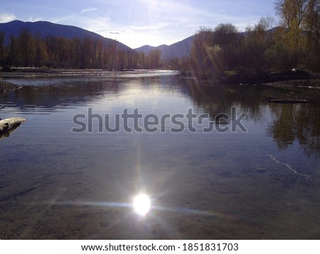 The sun reflecting in Kootenay river. Trees and the magnificent Rocky Mountains in the background. It's early springtime. In the nearance of Creston, British Columbia, Canada. 