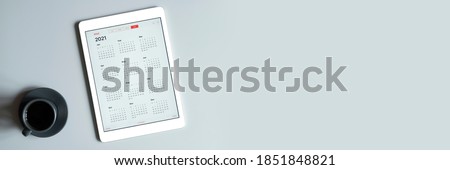 a tablet with an open calendar for 2021 year and a cup of coffee on a gray background. banner. space for text Royalty-Free Stock Photo #1851848821