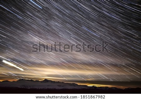 Colorful abstract night landscape with clouds and stars in the form of tracks in the moonlight in the sky over snowy mountains