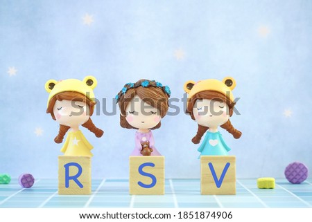 Three little girl toys with wood block RSV (Respiratory Syncytial Virus) on blue background. Children epidemic. Copy space.