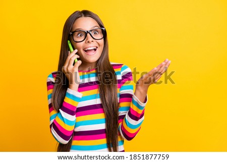Photo portrait of shocked happy girl talking on phone looking at empty space touching laughing isolated on bright yellow color background
