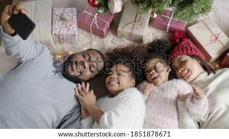 Candid happy black parents and little cute children african family having fun lying down on floor carpet at home holding mobile videocall online selfie with smile and laugh together.