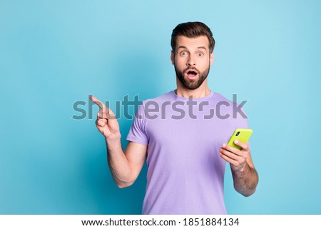 Photo portrait of amazed surprised man showing empty space keeping cellphone isolated vibrant blue color background