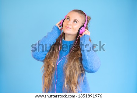 Beautiful young woman in headphones listening to music on blue background