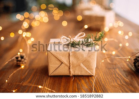 Craft wrapped present box on the wooden table with garland and fir branches