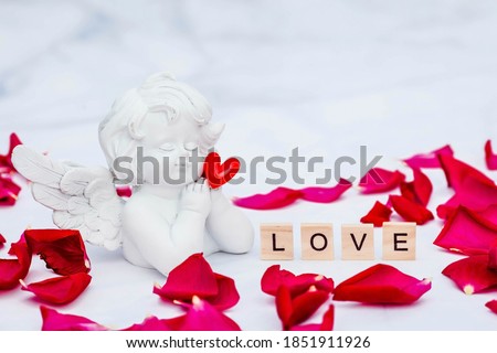 The word "Love" and a cute angel on a white, marble background. Love on wooden cubes. Theme of love. Valentine's day. Wooden blocks with the word love. Positive emotion.