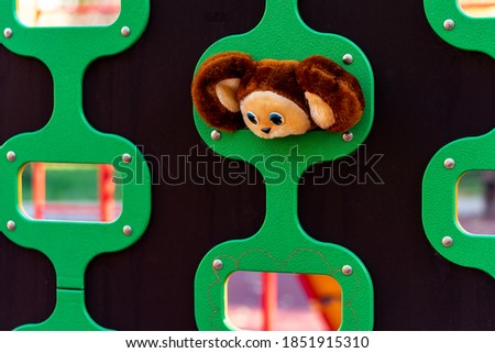 on a large dark stand, elliptical holes with green edging for kids climbing.  in one of the ellipses is the head of a plush toy with huge ears and blue eyes.