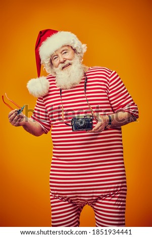 Joyful Santa Claus is relaxing and taking pictures in hot tropical countries. Christmas Holidays, tourist trips to the sea. Bright yellow background. 