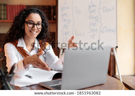 Online Education. Female English teacher having video conference chat with students and class group, using laptop. Woman wearing glasses and wireless earphones, talking to webcam, explaining Royalty-Free Stock Photo #1851963082