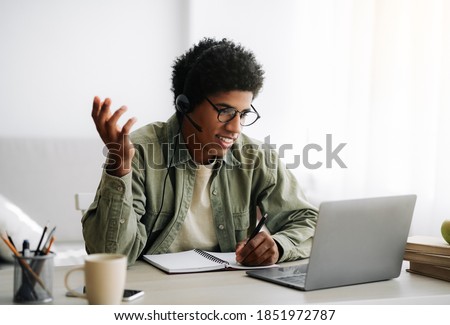 Online communication and web based learning. Positive black teenager speaking to his college tutor on laptop from home. Handsome African American student making video call on webcam