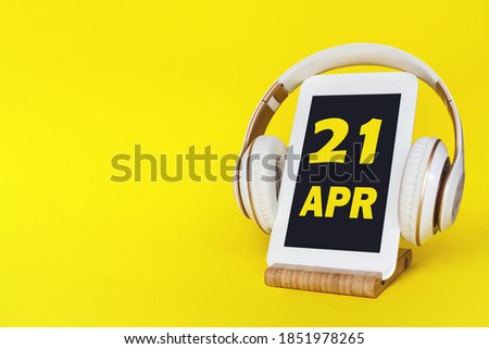 April 21st . Day 21 of month, Calendar date. Stylish headphones and modern tablet on yellow background. Space for text. Concept education, technology, lifestyle. Spring month, day of the year concept