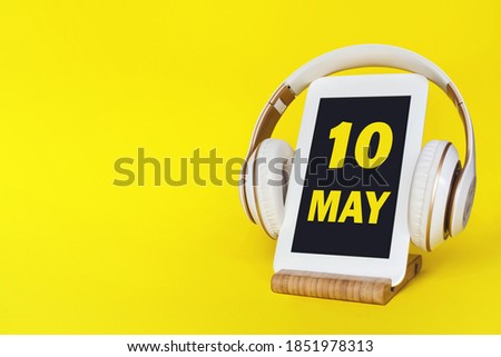 May 10th. Day 10 of month, Calendar date. Stylish headphones and modern tablet on yellow background. Space for text. Concept education, technology, lifestyle. Spring month, day of the year concept